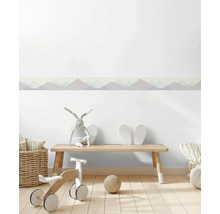 Zelfklevende behangrand met bergenmotief in een lichte kinderkamer met houten bankje en speelgoed.