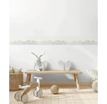 Zelfklevende behangrand met wolkenpatroon in een lichte kinderkamer met houten meubels en speelgoed.