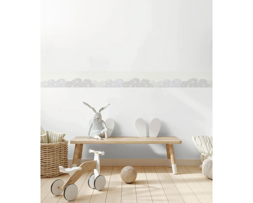 Zelfklevende behangrand met wolkenpatroon in een lichte kinderkamer met houten meubels en speelgoed.