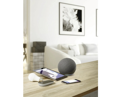 Foto van een woonkamer met smart home apparaten zoals luidspreker, tablet, smartphone en lamp op een tafel.