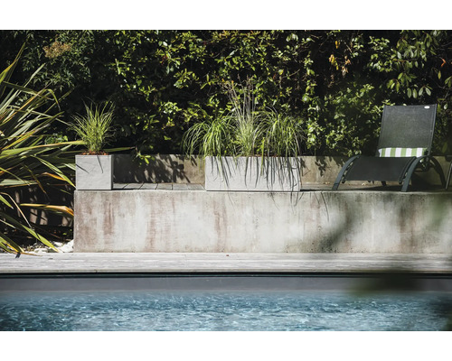 Betonnen plantenbakken met beplanting naast zwembad en ligstoel