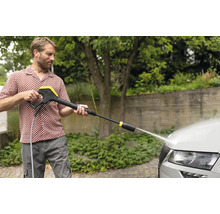 Man reinigt auto met hogedrukreiniger buitenshuis.