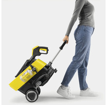 Vrouw trekt een geel-zwarte hogedrukreiniger met trolleyfunctie achter zich aan.