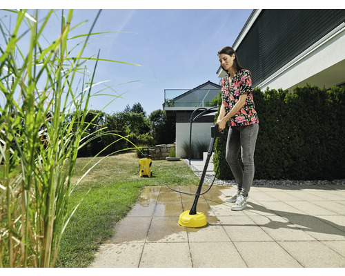 Vrouw reinigt terras met terrasreiniger en hogedrukreiniger in de tuin.