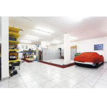 Ruime garage met werkbank, gereedschap, stellingen, kasten en een met een beschermhoes afgedekte auto