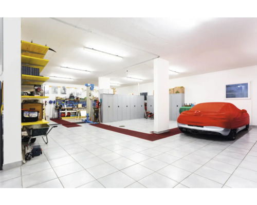 Ruime garage met werkbank, gereedschap, stellingen, kasten en een met een beschermhoes afgedekte auto