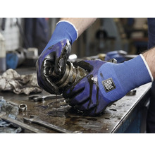 Een persoon houdt een vettig mechanisch onderdeel vast met werkhandschoenen.