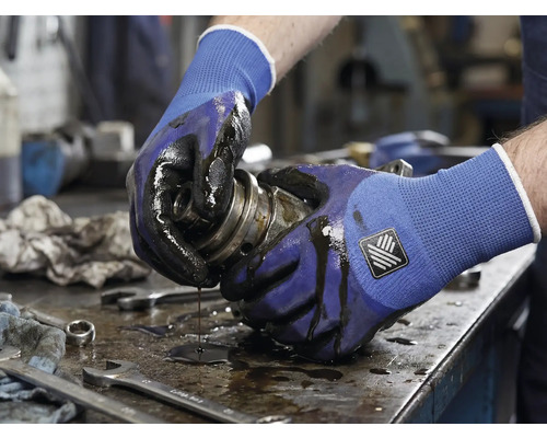 Een persoon houdt een vettig mechanisch onderdeel vast met werkhandschoenen.