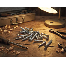 Werkplaatsopstelling met schroeven, schroevendraaier, tang, houtkrullen, gereedschapskist en lamp op een houten tafel