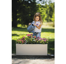 Meisje geeft bloemen water in een rechthoekige plantenbak in de tuin.