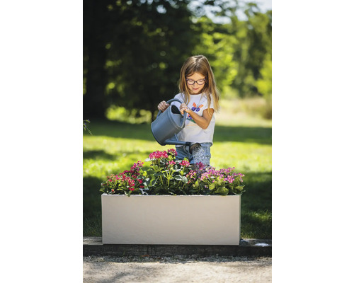 Meisje geeft bloemen water in een rechthoekige plantenbak in de tuin.