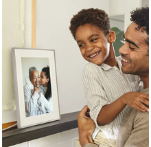 Digitale fotolijst op een plank, bekeken door een glimlachende vader en zoon.
