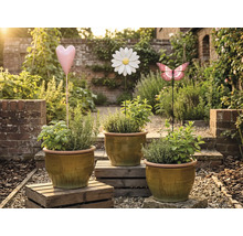 Drie plantenpotten met kruiden en decoratieve tuinpluggen in de vorm van een hart, bloem en vlinder in een tuin.