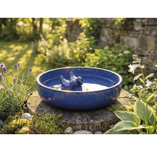 Blauwe vogeldrinkbak met vogelbeeldjes op boomstronk in de tuin