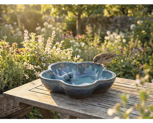 Keramische vogeldrinkbak met vogeldecoratie op houten tafel in de tuin