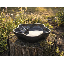 Keramische vogelbad met twee vogel figuren op een boomstronk in de tuin.