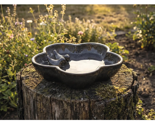 Keramische vogelbad met twee vogel figuren op een boomstronk in de tuin.