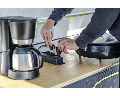 Iemand steekt een koffiezetapparaat in een stekkerdoos.