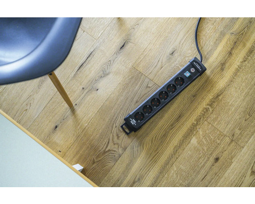 Meervoudig stopcontact op een houten vloer naast een stoel.