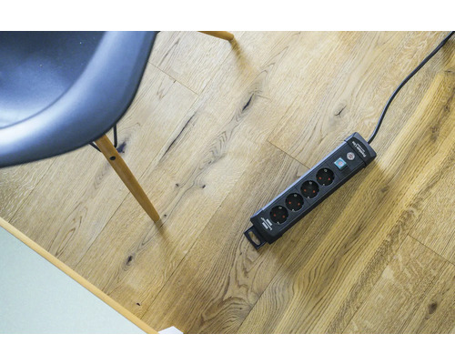 Verlengdoos met overspanningsbeveiliging en schakelaar op een houten vloer.