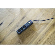 Verlengsnoer met drie stopcontacten en overspanningsbeveiliging op houten vloer