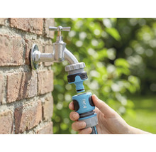 Tuinscène met waterkraan, hierop aangesloten een for_q tuinslangkoppeling in de hand