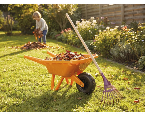 Tuinscene met kruiwagen, hark en kind dat bladeren verzamelt