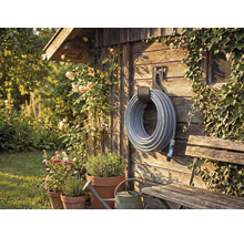 Tuinscène met slanghaspel aan houten wand, omgeven door planten