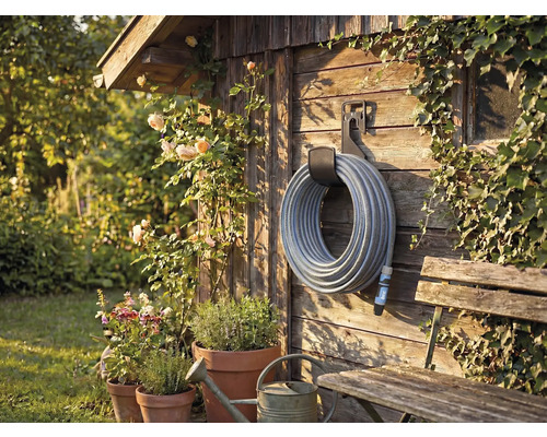 Tuinscène met slanghaspel aan houten wand, omgeven door planten