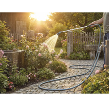 Een persoon bewater rozen met een tuinslang op een bestrate weg.