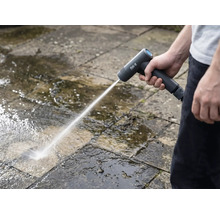 Een persoon reinigt stenen platen buitenshuis met een draadloze hogedrukreiniger.