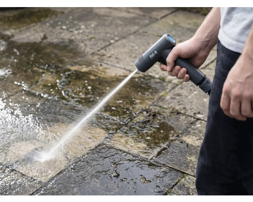 Een persoon reinigt stenen platen buitenshuis met een draadloze hogedrukreiniger.