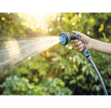 Hand houdt tuinslang met sproeikop vast tijdens het besproeien