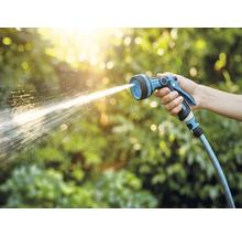 Een hand houdt een tuinspuit vast waar water uit spuit