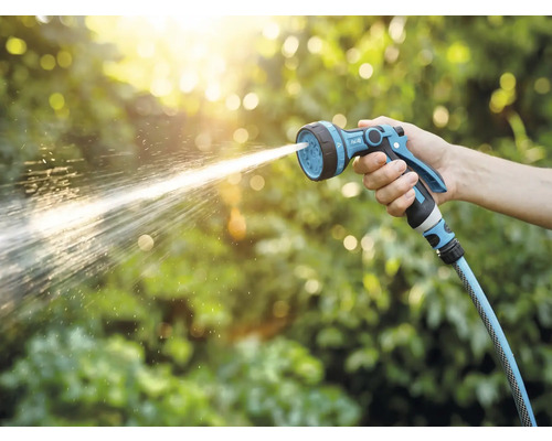 Een hand houdt een tuinspuit vast waar water uit spuit