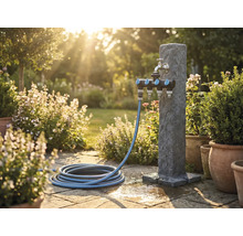 Tuinscene met waterzuil, meervoudige verdeler en tuinslang op stenen terras
