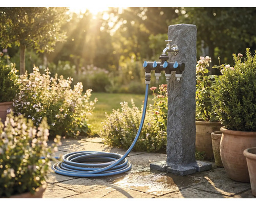 Tuinscene met waterzuil, meervoudige verdeler en tuinslang op stenen terras