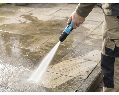 Een persoon reinigt een stenen terras met een for_q-tuinslang