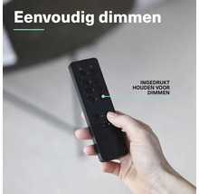 Een hand houdt een zwarte afstandsbediening vast met meerdere ronde knoppen voor het bedienen van de dimfunctie.