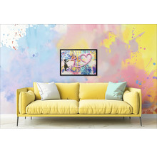 Gele bank met kussens voor een muur met een ingelijste afbeelding van een meisje en een hart