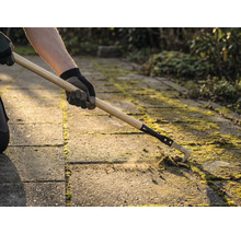 Iemand verwijdert mos tussen bestratingstenen met een voegenkrabber.