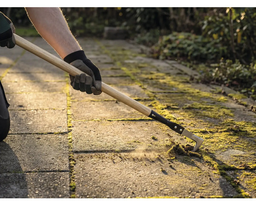 Iemand verwijdert mos tussen bestratingstenen met een voegenkrabber.