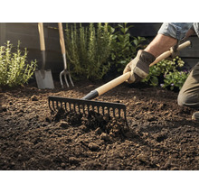 Tuinman harkt aarde met een hark, op de achtergrond zijn een spade en een riek te zien.