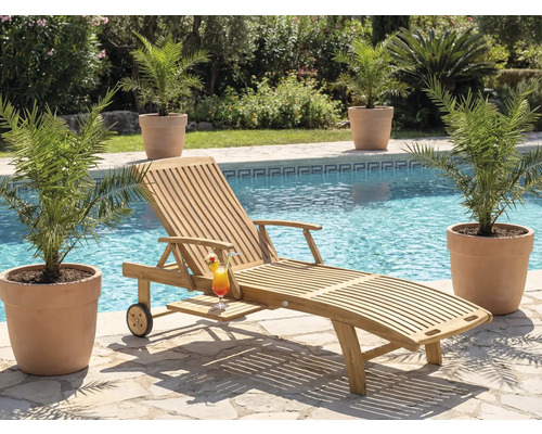 Scene met een houten ligstoel, een cocktail en planten bij een zwembad.