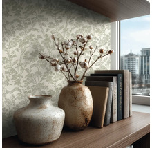 Vliesbehang met dennenpatroon in een lichte kamer met keramische vazen en boeken op een houten plank.