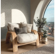 Lichte woonkamer met een houten fauteuil met zachte kussens, patroonbehang en kamerplanten voor een groot boograam.