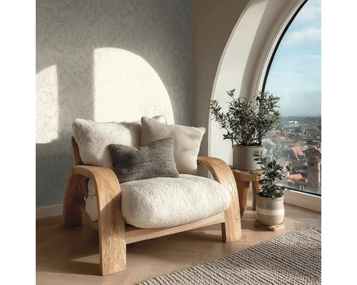 Lichte woonkamer met een houten fauteuil met zachte kussens, patroonbehang en kamerplanten voor een groot boograam.