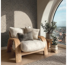 Lichte fauteuil met kussens naast kamerplanten en een raam