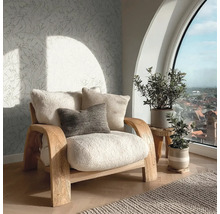 Uitnodigende woonkamer met houten fauteuil, pluizige kussens, vliesbehang met bladmotief en een groot rondboogvenster met uitzicht over de stad.