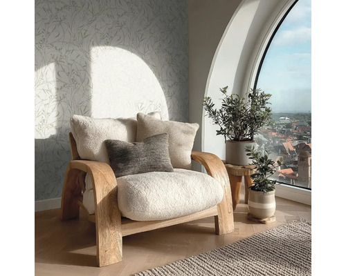 Uitnodigende woonkamer met houten fauteuil, pluizige kussens, vliesbehang met bladmotief en een groot rondboogvenster met uitzicht over de stad.